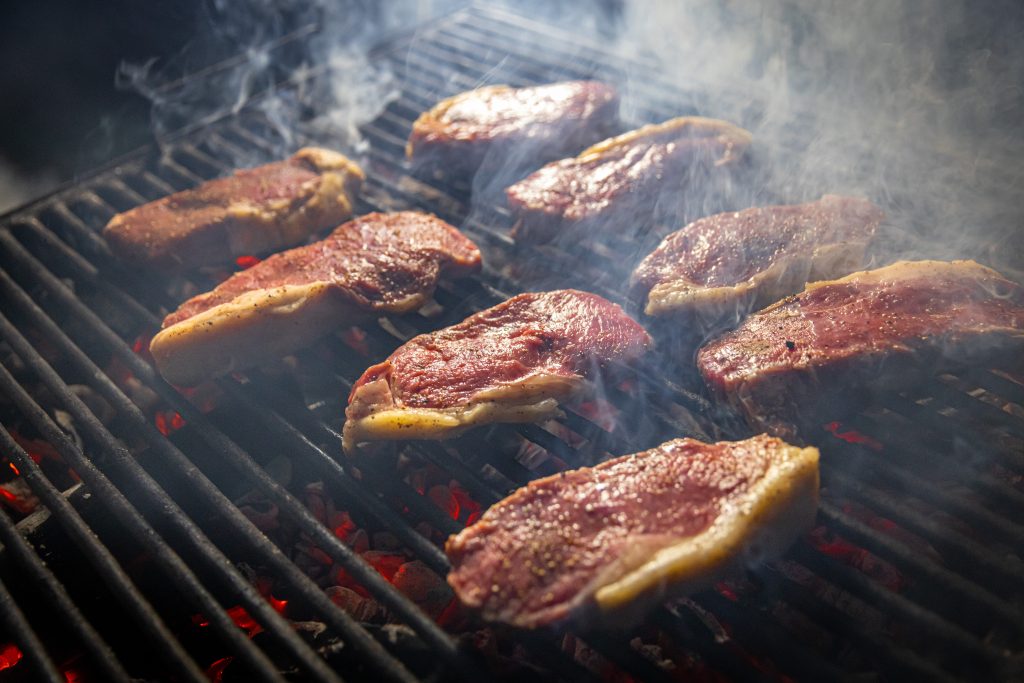 many steaks on a grill over hot coals