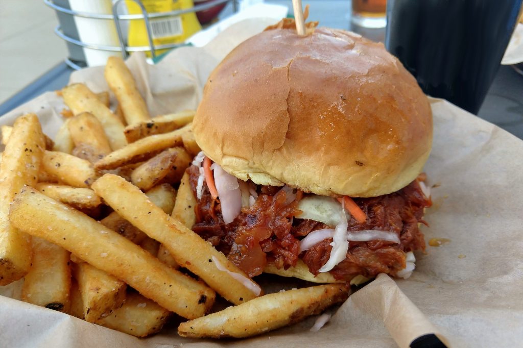 BBQ pulled pork sandwich with a side of fries on a plate outside