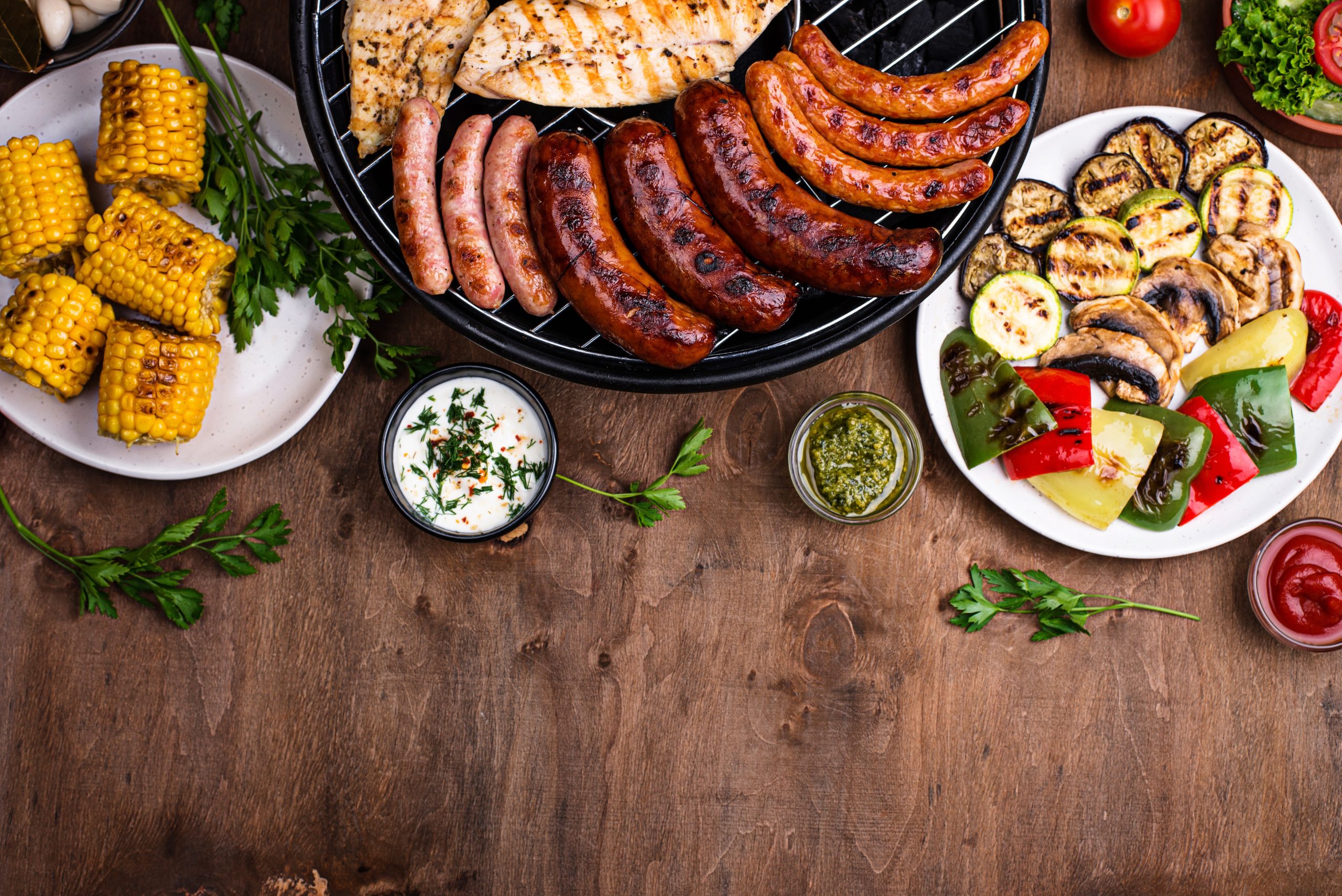 Grilled sausages, meat, and vegetables. up-close shot of BBQ food on wooden table